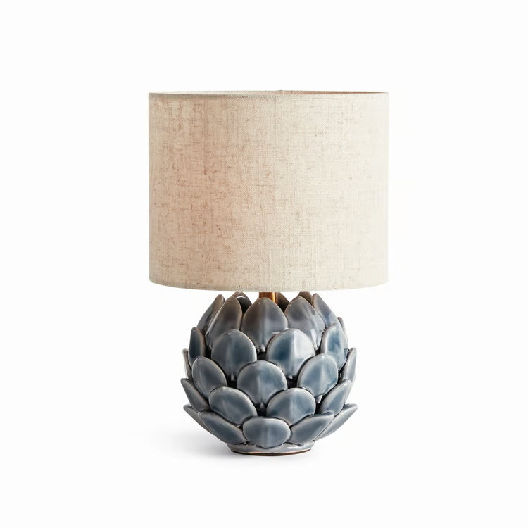 Table lamp with a textured blue base resembling an artichoke and beige lampshade on a white background