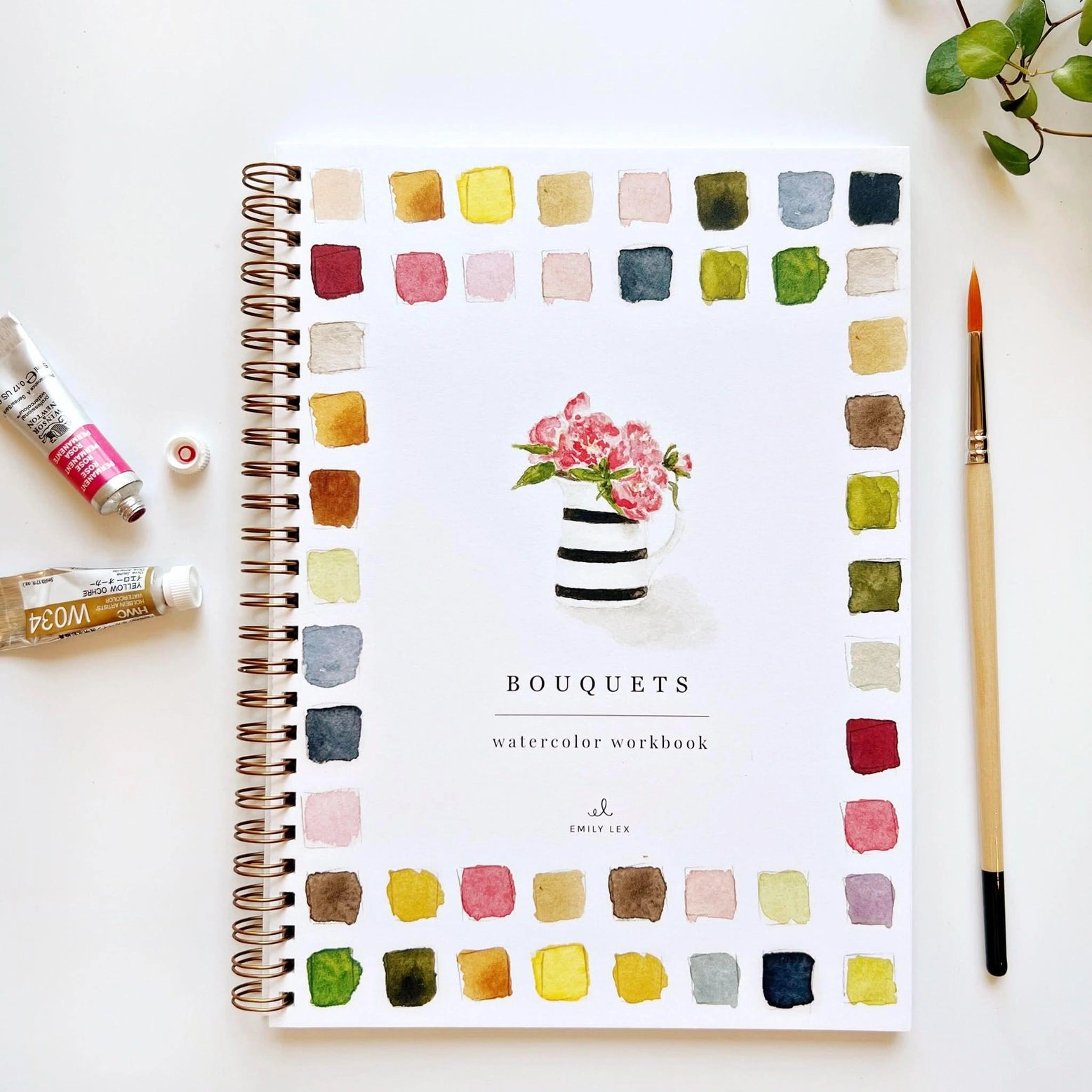 Bouquets watercolor workbook with color swatches and a striped vase with pink flowers on a white surface with art supplies.
