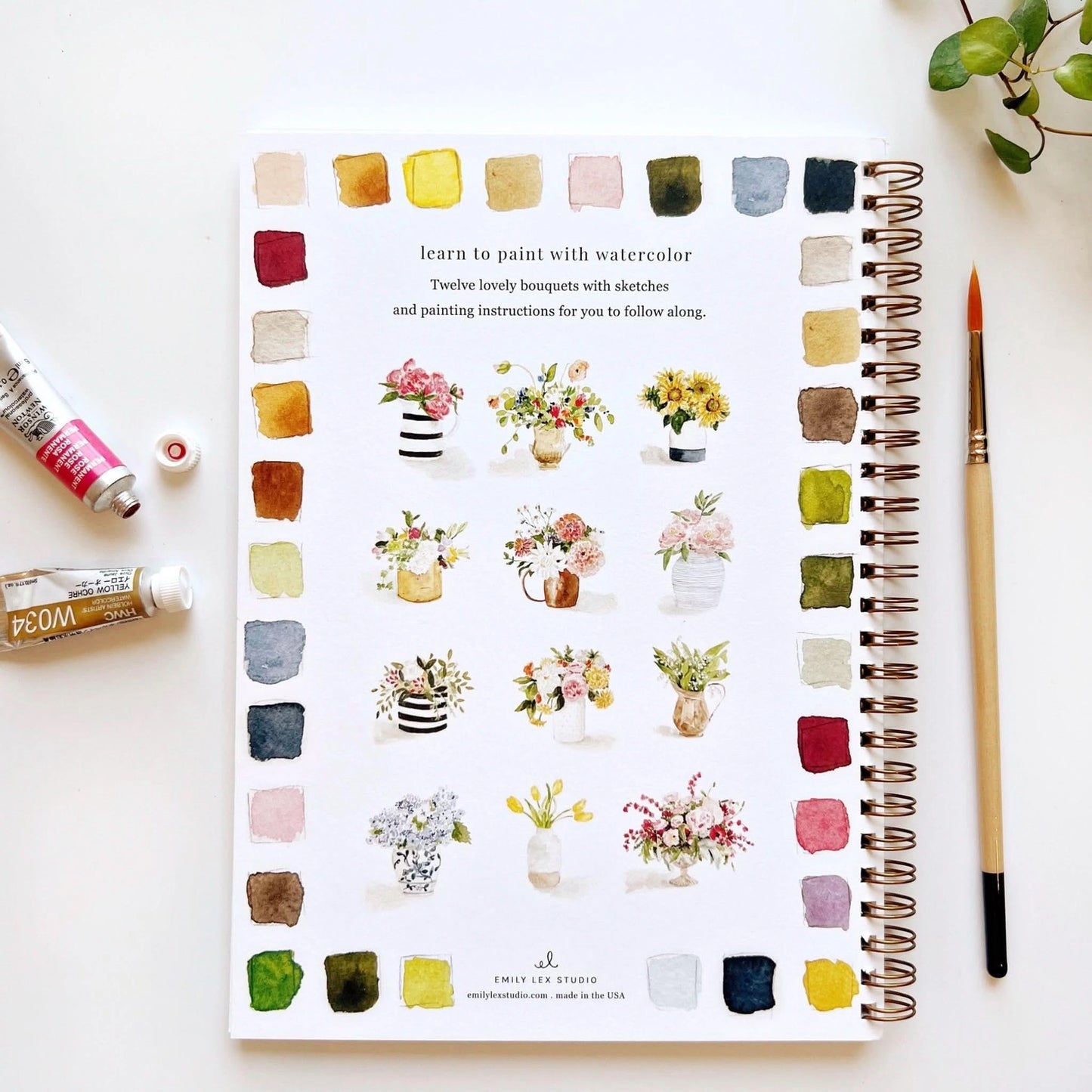 Notebook with watercolor bouquets and a paintbrush on a white surface