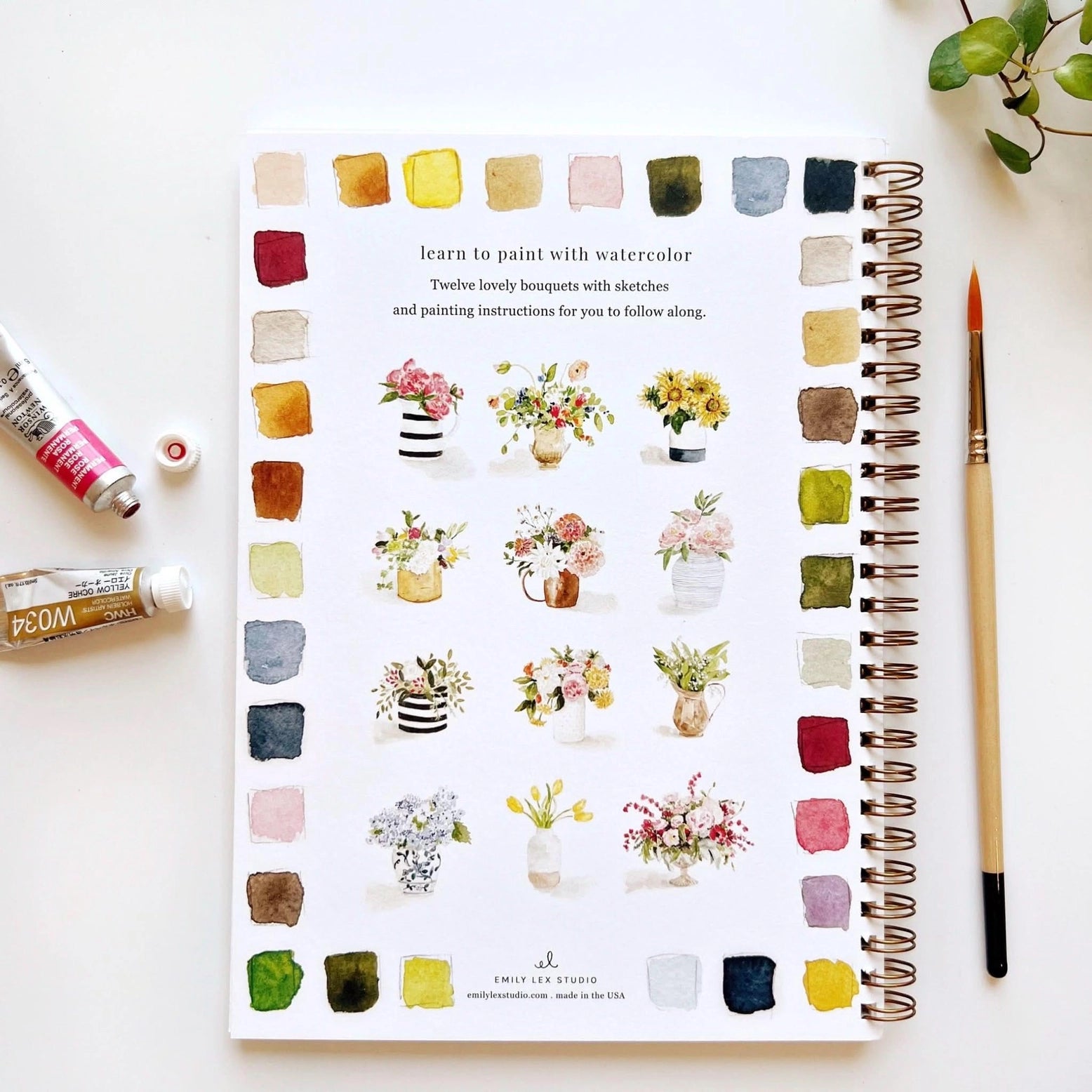 Notebook with watercolor bouquets and a paintbrush on a white surface