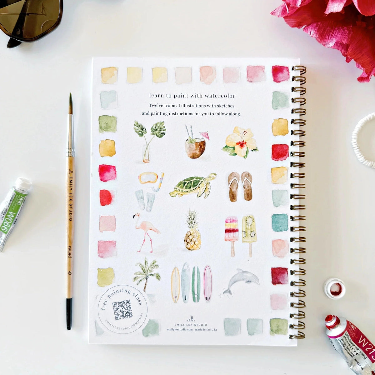 Artistic book with watercolor illustrations and paint swatches on a white surface with art supplies.
