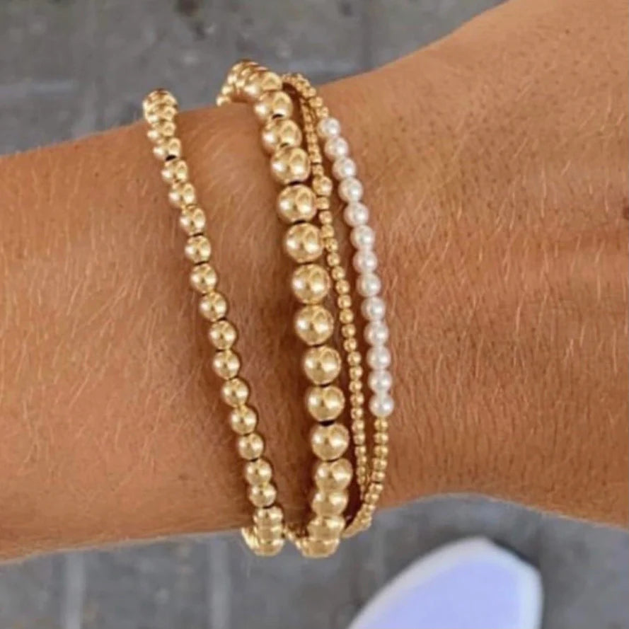A wrist with four enewton bracelets three gold beaded classic bracelets and one enewton Pearl and Gold Bliss Bracelet 