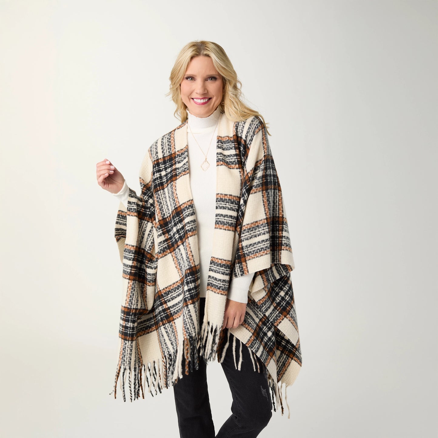 A woman modeling a black, cream and rust plaid fringed wrap over a black outfit, standing against a light gray studio background.t