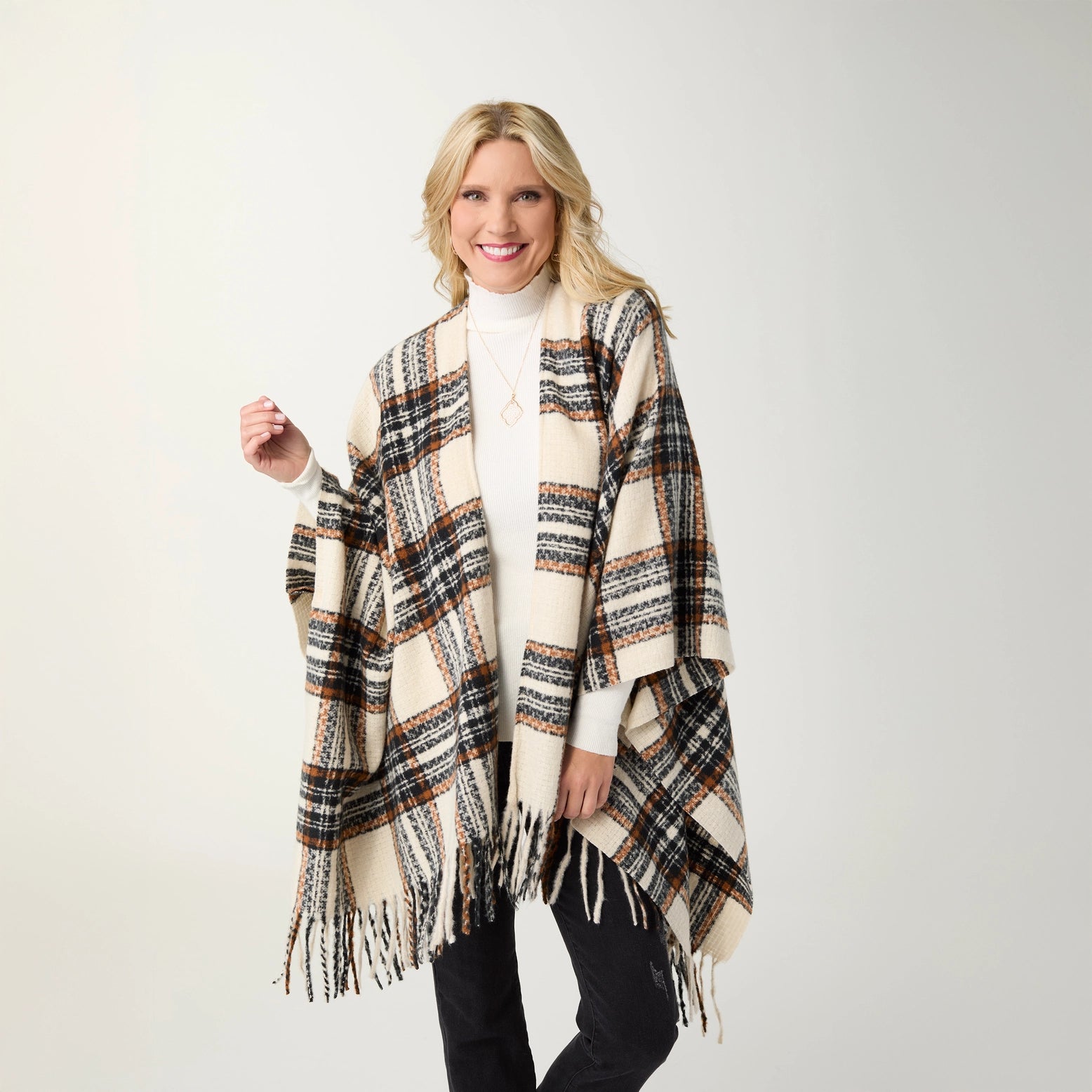 A woman modeling a black, cream and rust plaid fringed wrap over a black outfit, standing against a light gray studio background.t