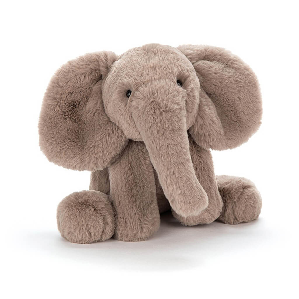 A plush toy elephant with warm grey-brown fur, bright black eyes, and large ears, sitting upright.