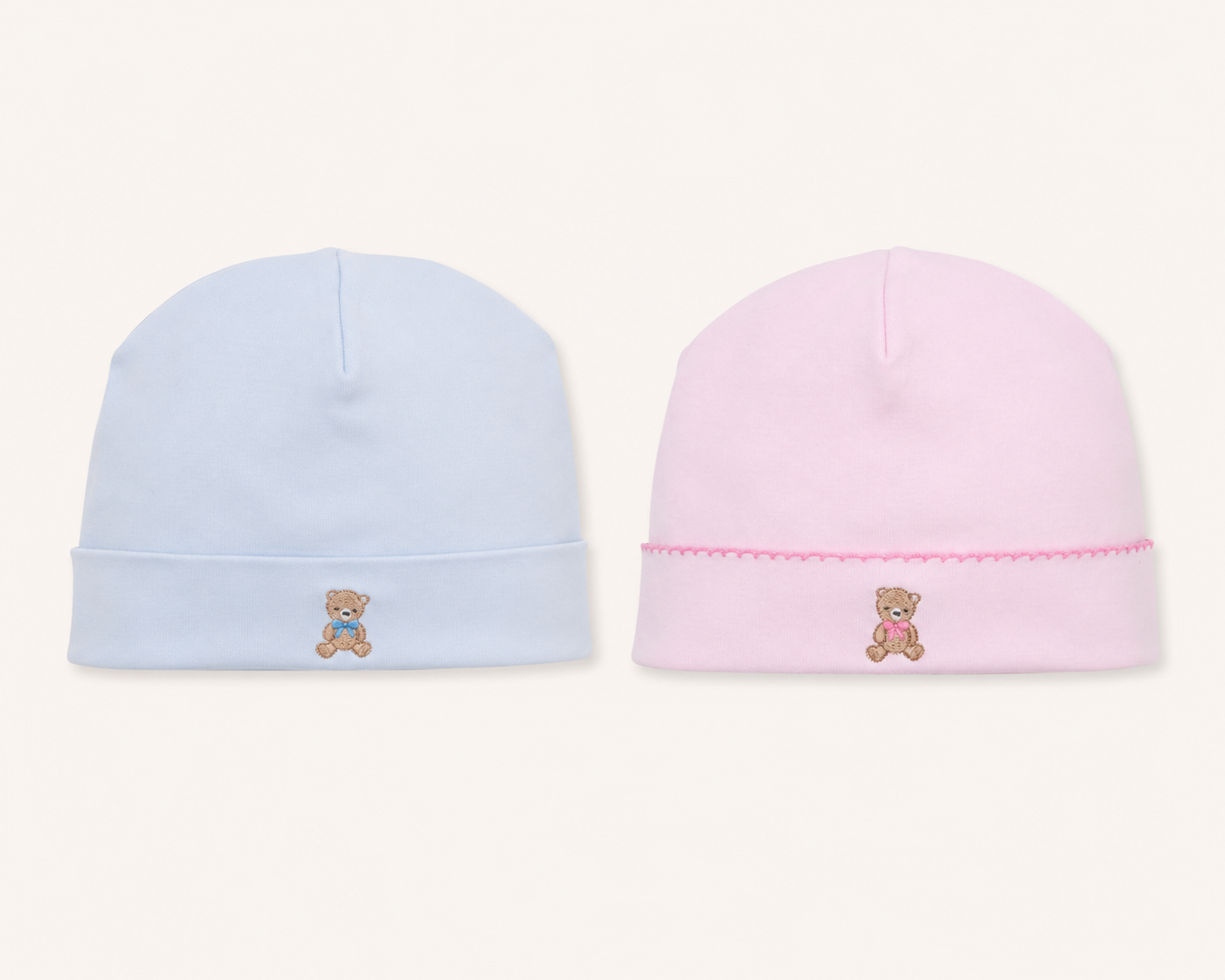 Two babykissy kissy teddy bear club beanie hats on a light cream background, one light blue with a small embroidered teddy bear and the other light pink with a matching pink embroidered teddy bear and decorative pink stitched trim.