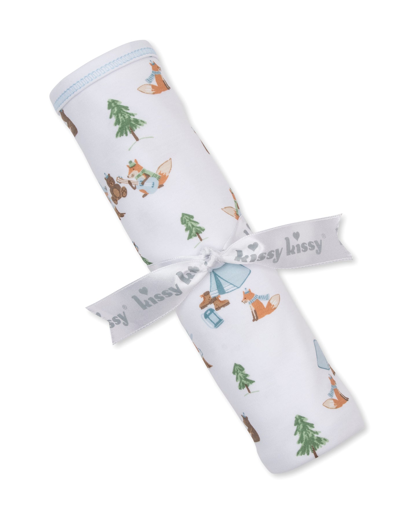 A rolled white baby blanket with a woodland print of foxes, trees, and a tent, tied with a white ribbon that reads 'kissy kissy'.