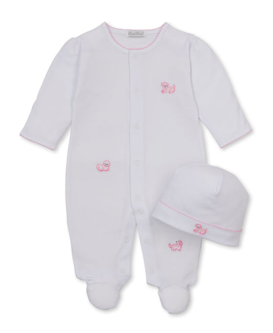 A white baby footed sleeper with long sleeves and a matching white beanie hat, both featuring small pink embroidered puppy motifs and pink trim, displayed on a clean white background.