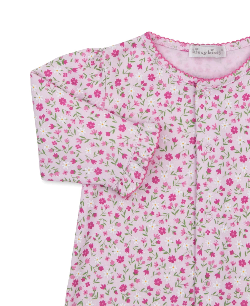A close-up of a long-sleeve baby top by Kissy kissy, featuring a pink and white floral print with green stems and a scalloped neckline.