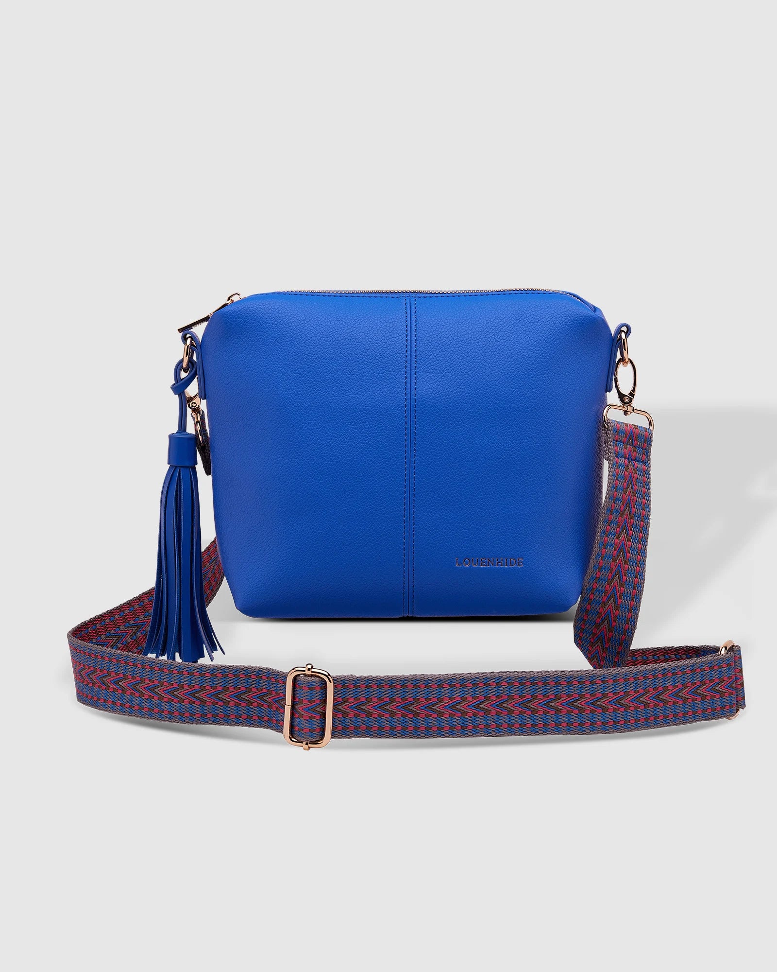 A blue Louenhide Kasey Crossbody Bag with a geometric patterned strap and a tassel, displayed against a white background.