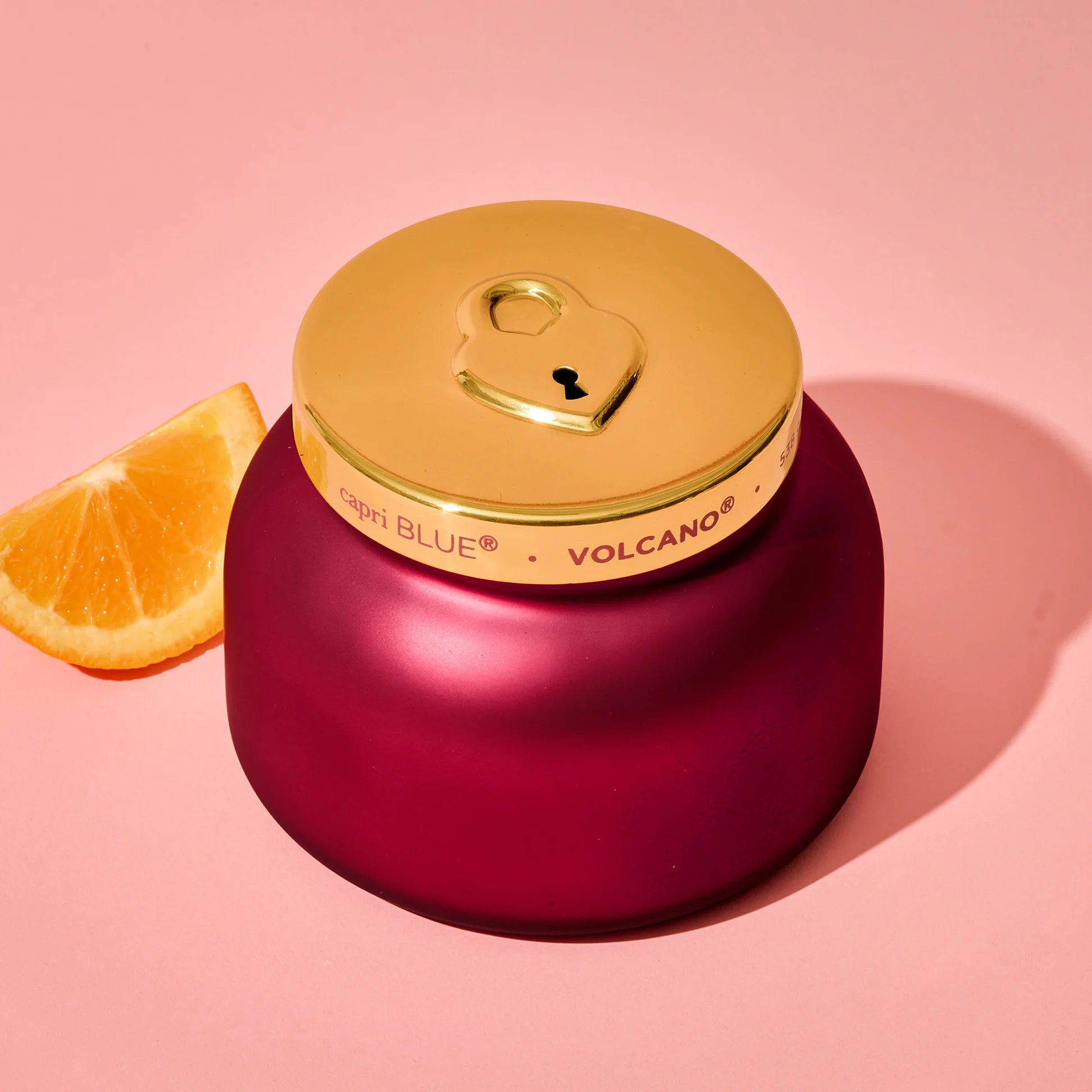 Red candle with gold lid with an outline of a lock on a pink background