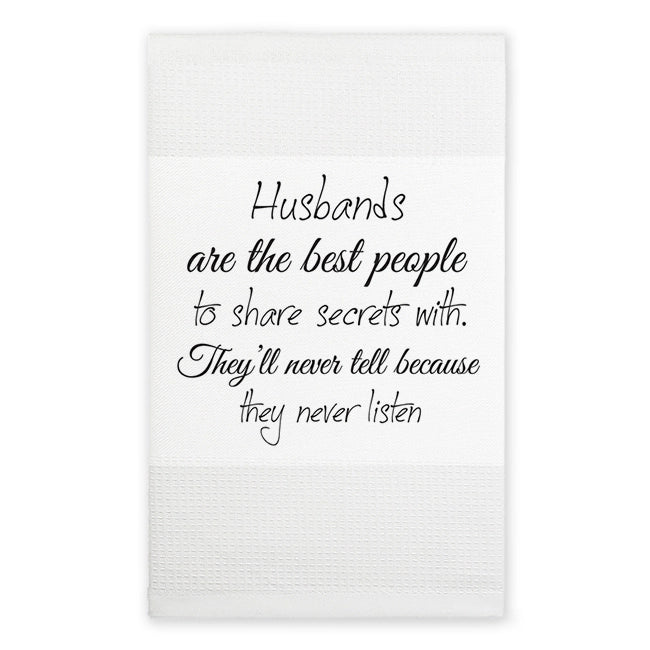A white kitchen towel with a humorous quote printed in black cursive text that reads, 'Husbands are the best people to share secrets with. They'll never tell because they never listen.
