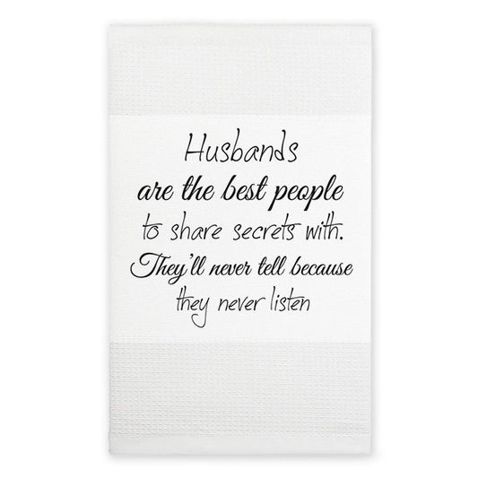 A white kitchen towel with a humorous quote printed in black cursive text that reads, 'Husbands are the best people to share secrets with. They'll never tell because they never listen.