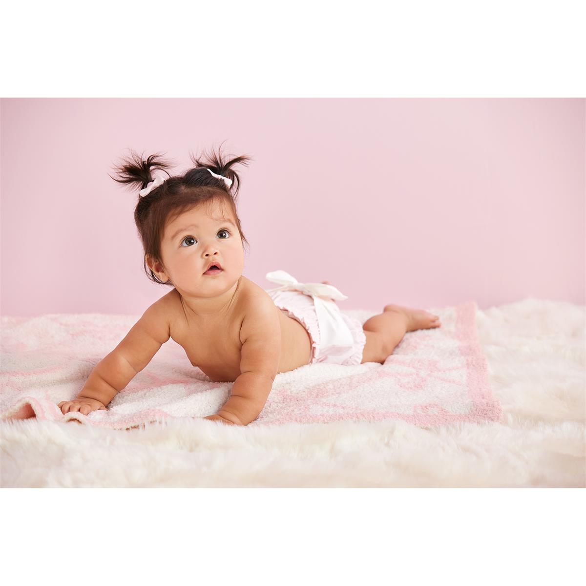 Baby lying on a fluffy pink blanket  with mudpie pink diaper cover with a whit bow on a pink background