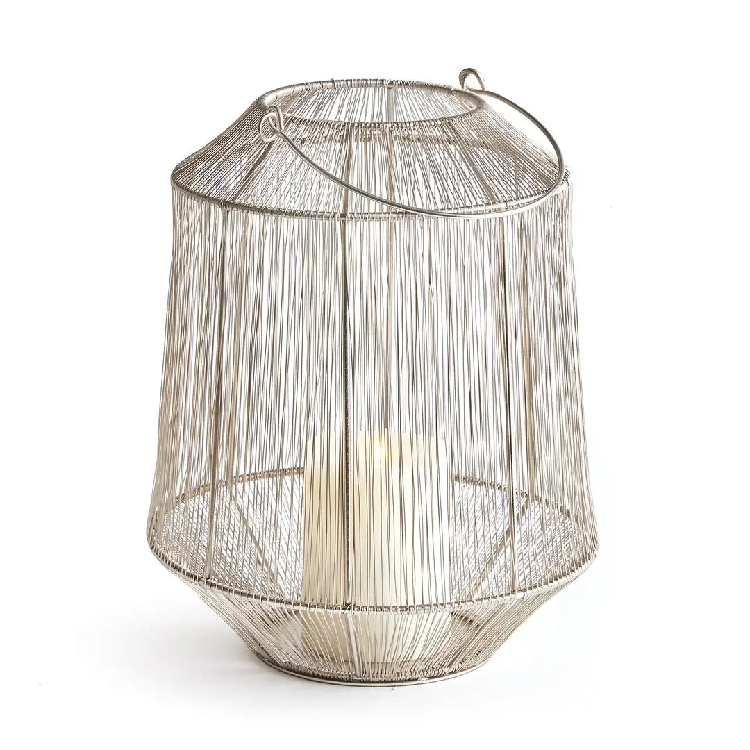 A silver-toned metal wire lantern with a tapered cylindrical shape, featuring a top handle and a lit candle inside, set against a plain white background.