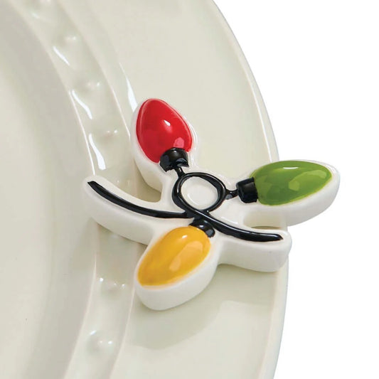 A nora fleming mini-Christmas three-light holiday string, featuring red, green, and yellow, bulbs with black wire details, resting on a white ceramic plate.