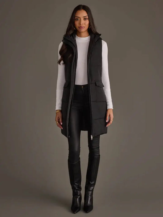 Woman wearing a long black vest by Panache over a white shirt with black pants and boots on a gray background