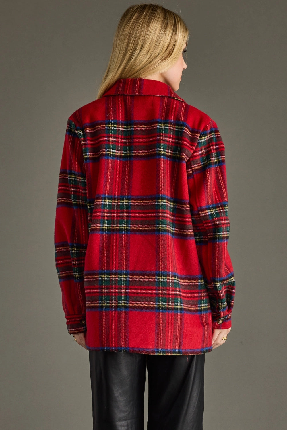 A woman shown from the back wearing a red plaid button-up shirt with black leather pants, photographed against a solid dark gray studio background.