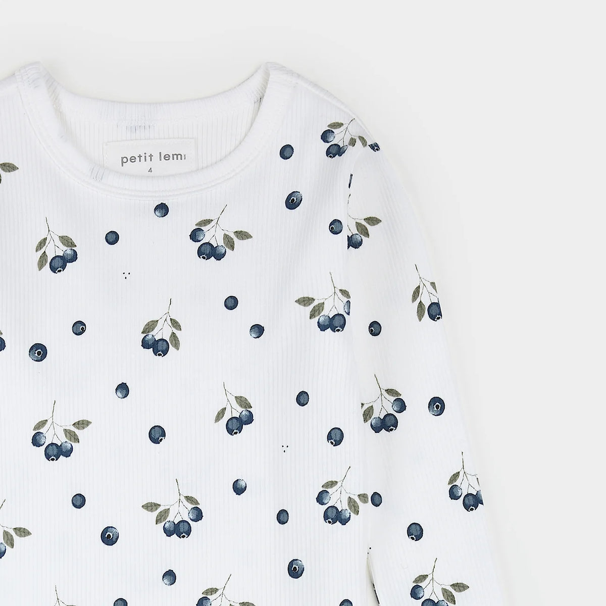 A close-up of a white ribbed long-sleeve top with an allover print of blueberries and green leaves. The brand label 'petit lem.
