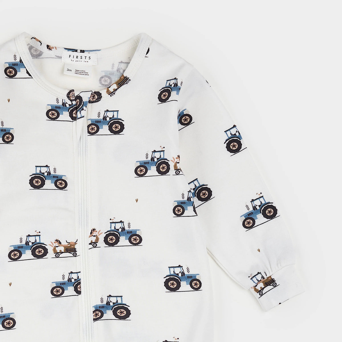 A baby footed one-piece sleeper in white, featuring an all-over print of blue tractors and small brown animals