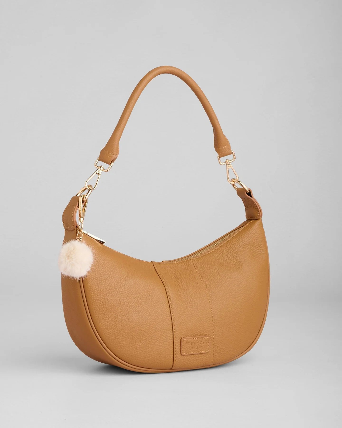 pom pom london sutton sling bag in a maple color and a beige pom pom