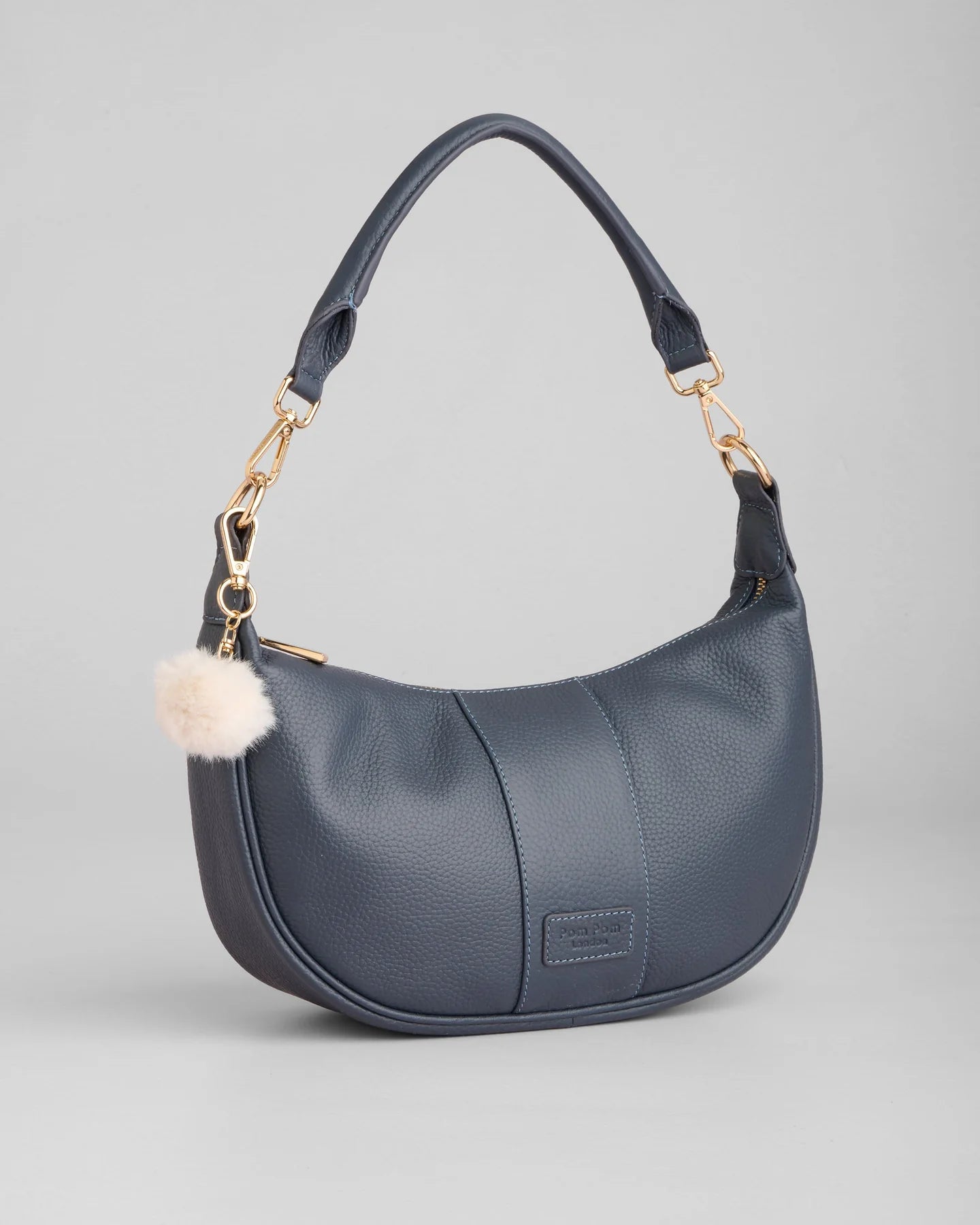pom pom london sutton sling bag in slate blue with a cream pom pom