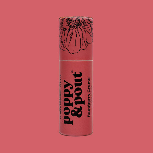 A single tube of poppy & pout Raspberry Creme lip balm standing upright against a solid pink background. The tube is a dusty rose pink with black text and a black line-art illustration of a poppy flower on the cap.