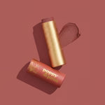 poppy and pout debbie lip tint Makeup stick with gold cap and red casing on a maroon background