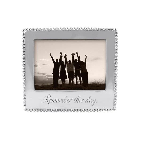 A silver picture frame with a beaded border and the engraved phrase 'Remember this day.' The center is filled with a sepia-toned photo of five people standing with raised arms.