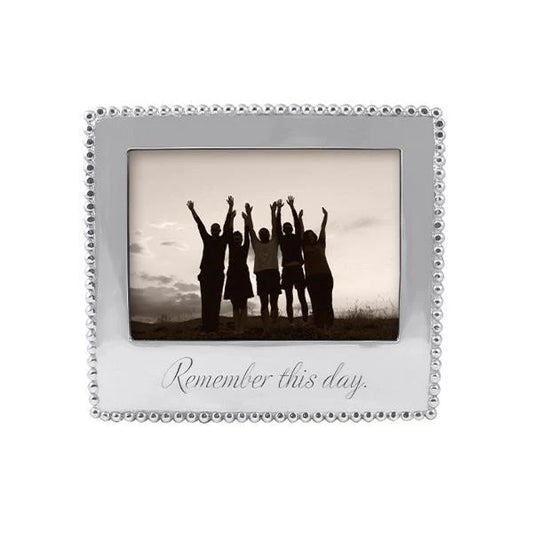 A silver picture frame with a beaded border and the engraved phrase 'Remember this day.' The center is filled with a sepia-toned photo of five people standing with raised arms.