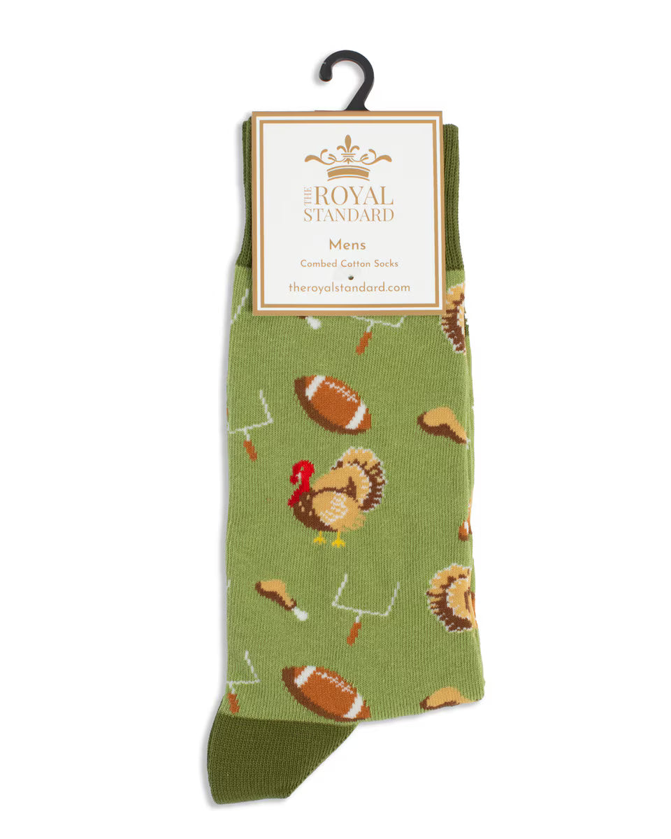 A pair of green crew socks with a pattern of footballs, turkeys, and drumsticks, hanging from a black plastic hook with a white paper label that reads 'The Royal Standard'.