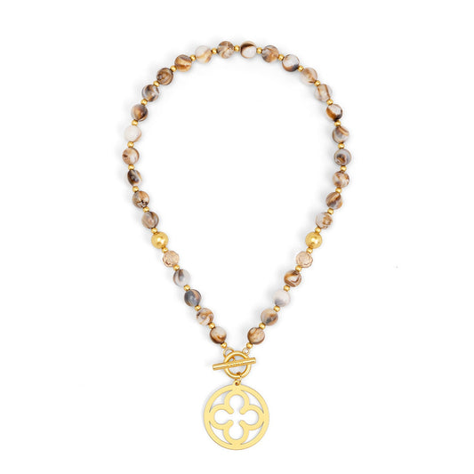 A beaded necklace featuring brown and beige marbled beads with small gold spacer beads, finished with a gold toggle clasp and a circular gold pendant with a quatrefoil cutout design.