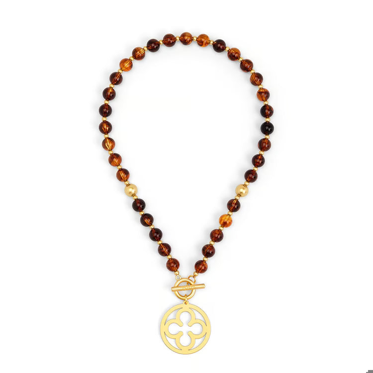 A beaded necklace featuring translucent amber and dark brown glass beads, accented with small gold spacer beads and a gold-tone toggle clasp with a circular cutout pendant.